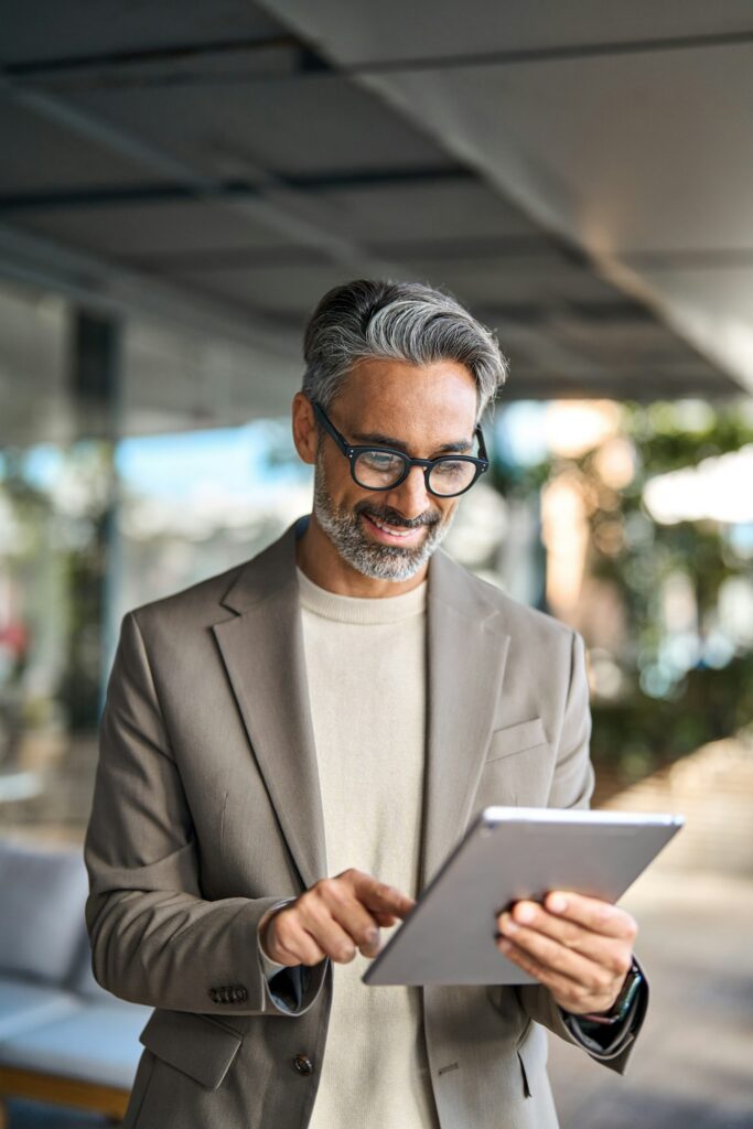 Busy happy older business man standing outdoors using digital tablet. Vertical.